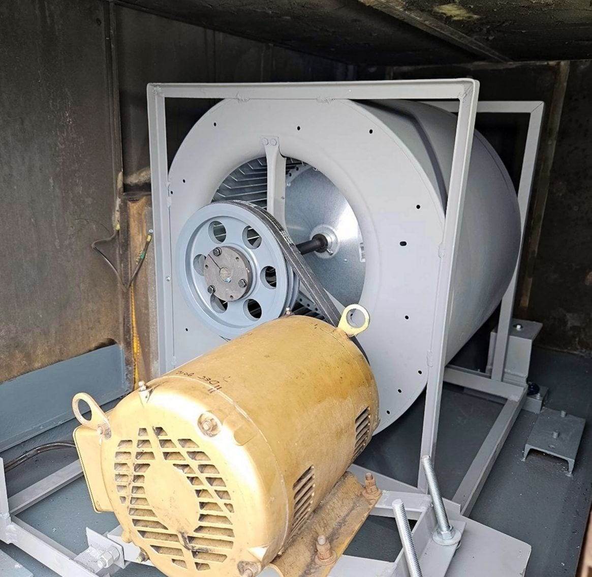 Belt-driven blower wheel in a gray housing with a large yellow electric motor, pulley and belt, mounted on a frame inside an air-handler cabinet
