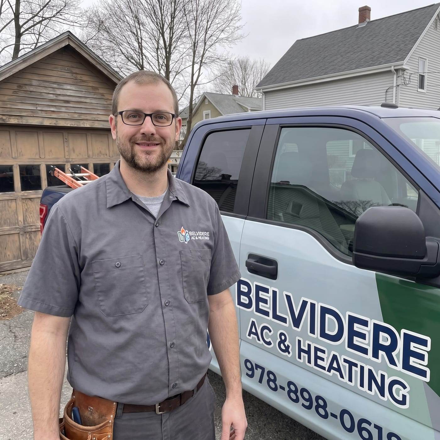 Bobby Williamson, manager of Belvidere AC & Heating, smiling in a gray company work shirt with a leather tool pouch, standing beside the lettered service truck
